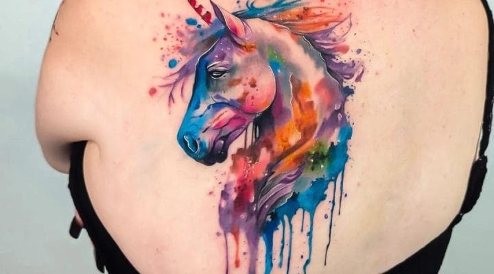 Watercolour unicorn tattoo with multicoloured splashes on the upper back