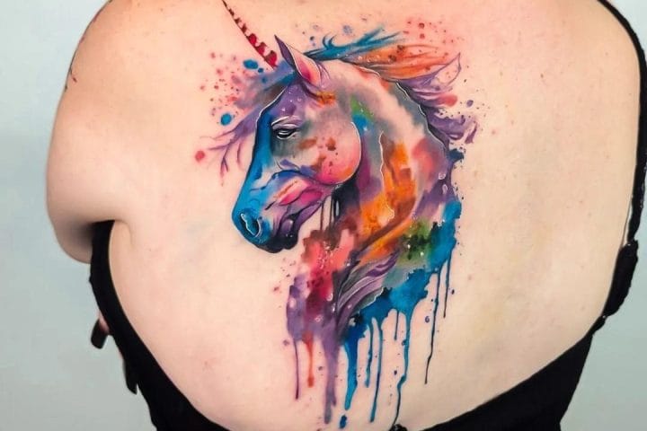 Watercolour unicorn tattoo with multicoloured splashes on the upper back
