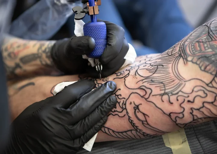 Tattoo artist wearing black gloves outlining a tattoo on an arm