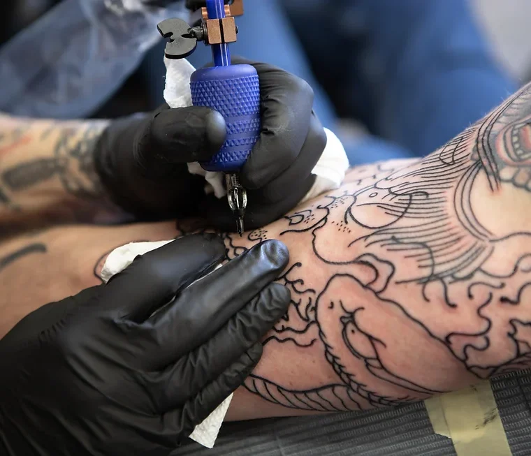 Tattoo artist wearing black gloves outlining a tattoo on an arm