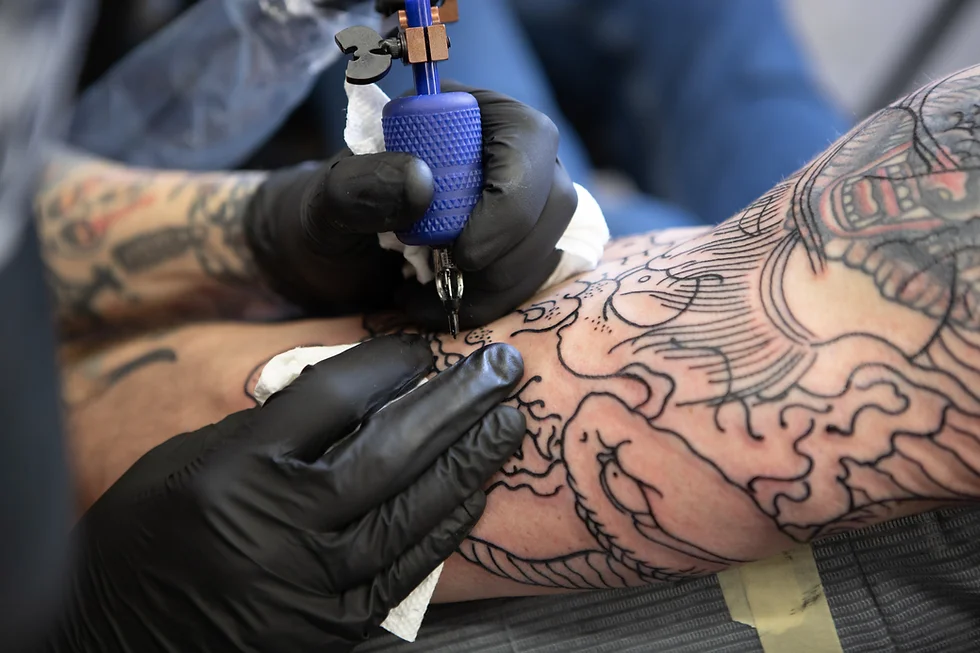 Tattoo artist wearing black gloves outlining a tattoo on an arm