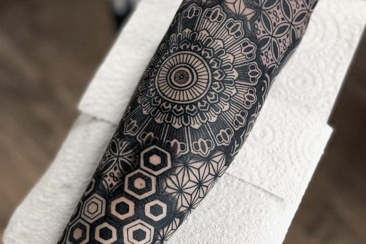 Black geometric forearm tattoo combining a circular mandala and repeating patterns