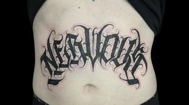 Bold black ornamental lettering tattoo across the abdomen