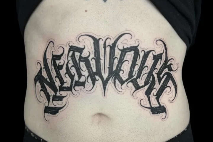 Bold black ornamental lettering tattoo across the abdomen