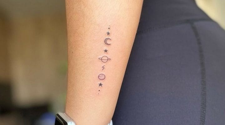 Fine line forearm tattoo with small stars, a crescent moon and planets