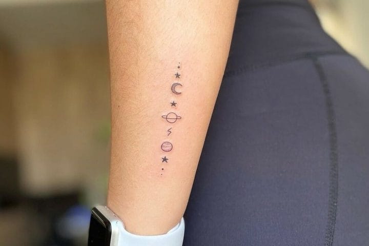 Fine line forearm tattoo with small stars, a crescent moon and planets