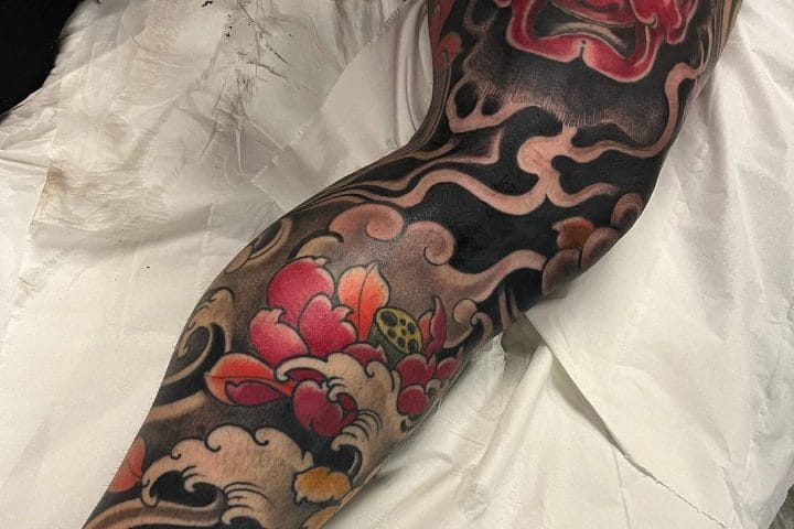 Japanese-style sleeve tattoo with a red mask, flowers and black waves