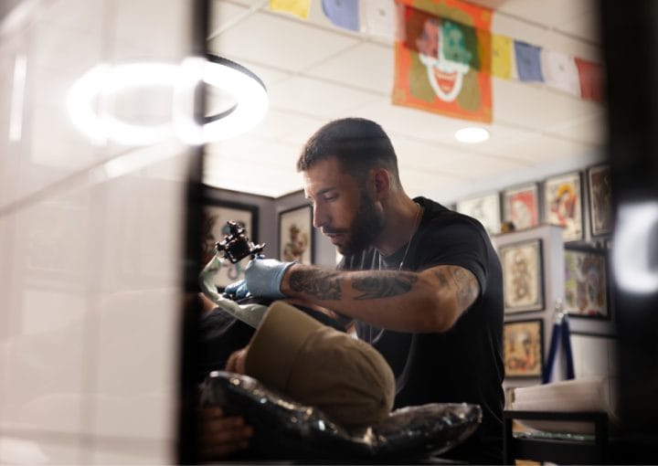 Tattoo artist wearing blue gloves working with a client in a studio