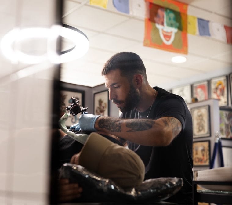 Tattoo artist wearing blue gloves working with a client in a studio