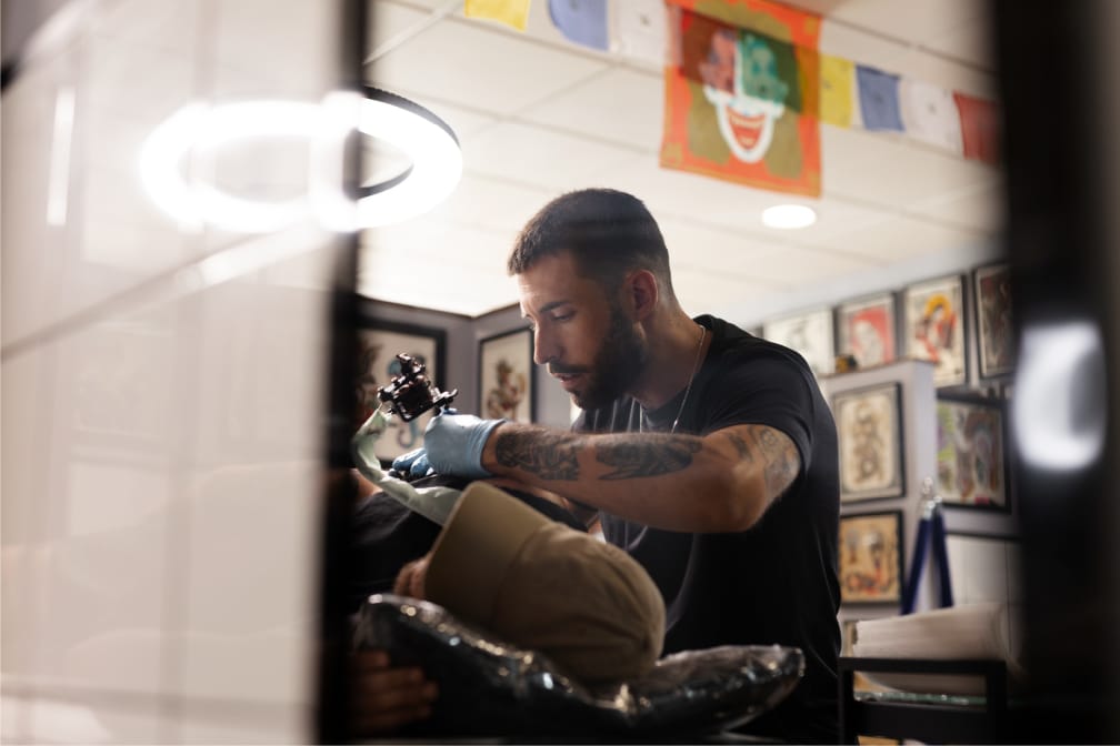 Tattoo artist wearing blue gloves working with a client in a studio