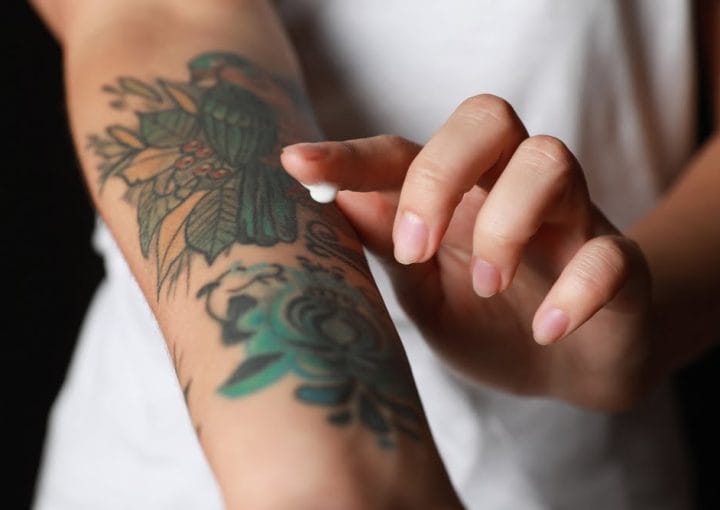Applying moisturiser to colourful tattoos on a forearm