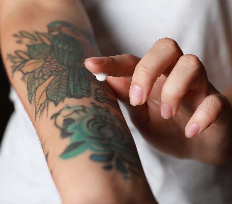 Applying moisturiser to colourful tattoos on a forearm