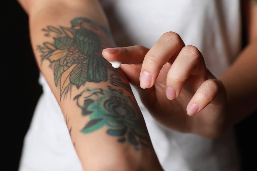 Applying moisturiser to colourful tattoos on a forearm