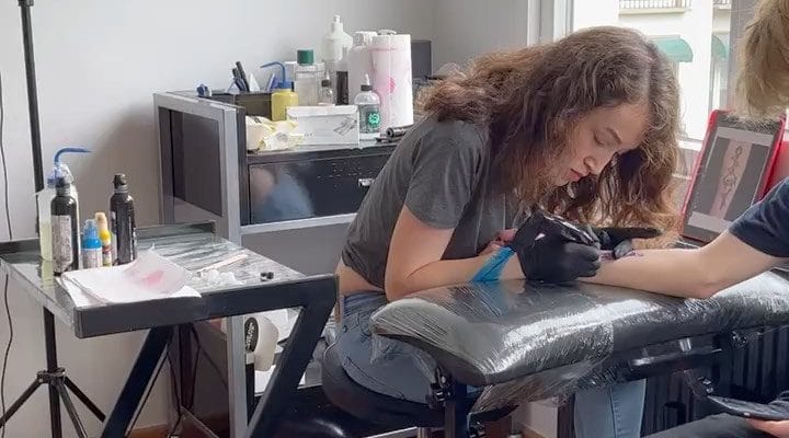 Tattoo artist working on a client’s forearm beside a studio window